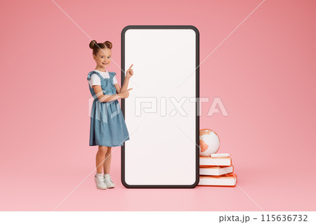 Online Study. Cute schoolgirl pointing at large smartphone touchscreen on pink background showing blank screen mockup for educational application advert. Collage with books and world globe icon, 115636732