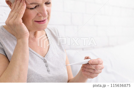 Senior woman is seen holding a thermometer in her hand, likely checking her temperature for any signs of fever or illness, closeup Senior woman is seen holding a thermometer in her hand, likely checking her temperature for any signs of fever or illness, closeup 115636875