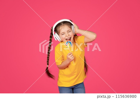 Carefree Preteen Female Child Singing With Lollipop In Hands, Cheerful Little Girl Wearing Wireless Headphones Holding Colorful Candy, Having Fun Over Pink Studio Background, Enjoying Music 115636980