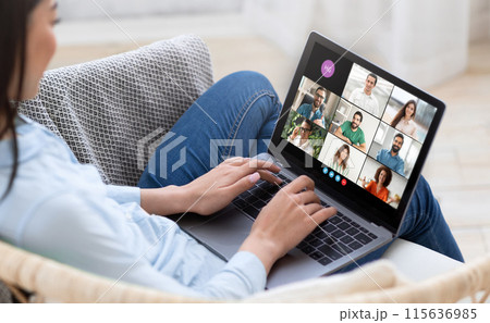 A woman is sitting on a couch, engaging in a virtual meeting with multiple participants displayed on her laptop screen. She appears focused and involved in the discussion A woman is sitting on a couch, engaging in a virtual meeting with multiple participants displayed on her laptop screen. She appears focused and involved in the discussion 115636985