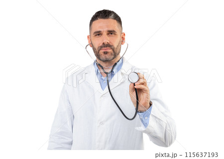 A man doctor, dressed in a white coat, holds a stethoscope against a plain white background. He appears focused, possibly preparing for a medical check-up or consultation. 115637193