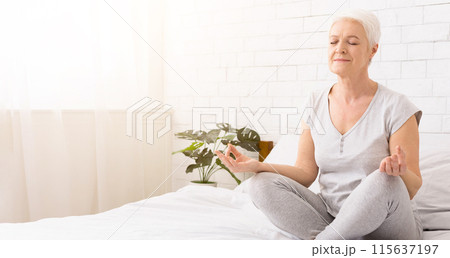 Keep calm and breath. Senior woman meditating in lotus position on bed, padmasana, free space 115637197