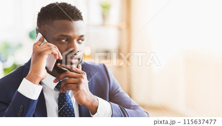 Young african entrepreneur having pleasant conversation with business partner by phone, office interior, copy space 115637477