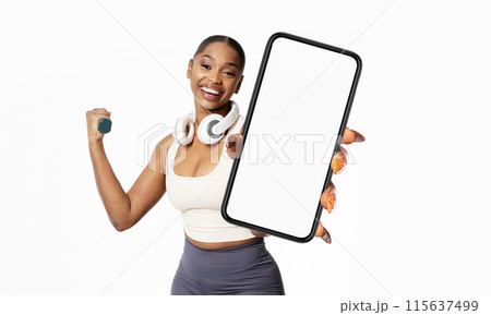 African American young woman with a joyful expression is holding a large smartphone with a blank screen towards the camera. African American young woman with a joyful expression is holding a large smartphone with a blank screen towards the camera. 115637499