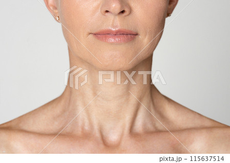 Cropped of a womans neck and chin. The woman is wearing a light color shirt and has a neutral expression. Her skin is smooth and wrinkle-free. 115637514