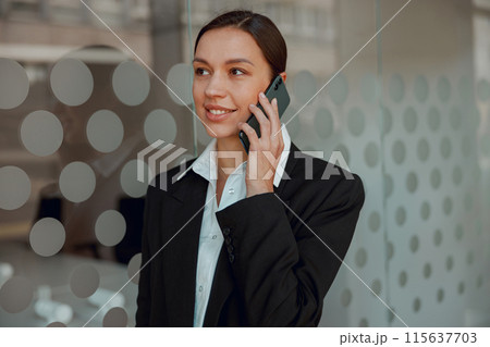 Businesswoman in formal attire talking on the phone at a modern office environment Businesswoman in formal attire talking on the phone at a modern office environment 115637703