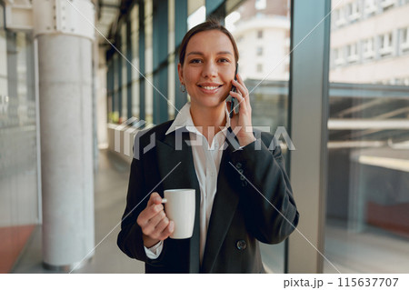 A modern office setting with a young professional woman holding coffee and talking on the phone A modern office setting with a young professional woman holding coffee and talking on the phone 115637707