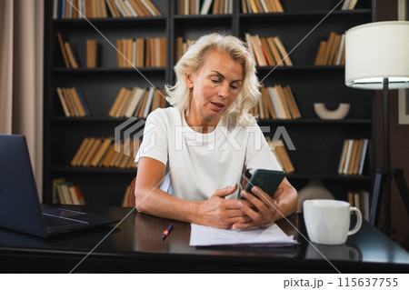 Confident stylish European middle aged senior woman using smartphone at workplace. Stylish older mature 60s lady businesswoman with cell phone in office. Boss leader using internet apps Confident stylish European middle aged senior woman using smartphone at workplace. Stylish older mature 60s lady businesswoman with cell phone in office. Boss leader using internet apps 115637755
