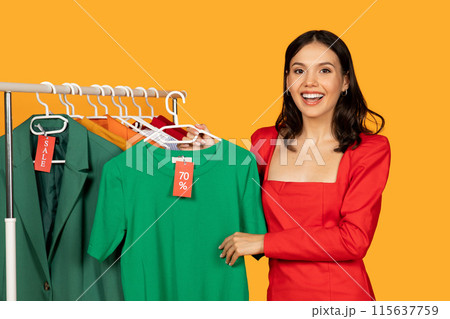 A woman is standing next to a metal rack filled with various clothing items indoors. She appears to be browsing through the garments, possibly shopping for new clothes A woman is standing next to a metal rack filled with various clothing items indoors. She appears to be browsing through the garments, possibly shopping for new clothes 115637759