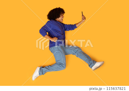 A man is mid-air, captured while jumping energetically with one hand holding a cell phone. His body is in motion, creating a dynamic and active scene. A man is mid-air, captured while jumping energetically with one hand holding a cell phone. His body is in motion, creating a dynamic and active scene. 115637821