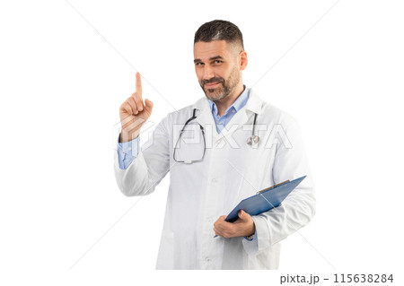 A man doctor dressed in a white lab coat stands confidently with one hand holding a clipboard and the other hand pointing upward. The background is a clean, white studio setting A man doctor dressed in a white lab coat stands confidently with one hand holding a clipboard and the other hand pointing upward. The background is a clean, white studio setting 115638284