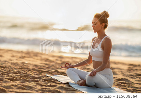 Young european woman enjoy workout, spare time, vitality, doing breathing exercises and practice yoga in lotus position on sea beach, free space. Meditation, hobby outdoor Young european woman enjoy workout, spare time, vitality, doing breathing exercises and practice yoga in lotus position on sea beach, free space. Meditation, hobby outdoor 115638364