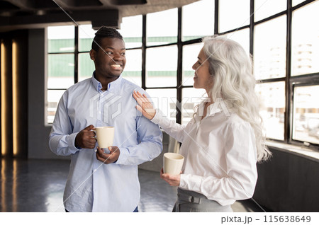 Corporate Lifestyle And Communication. Multiethnic Business Colleagues Enjoying Coffee Break, Talking Holding Mugs, Lady Touching Man's Shoulder Communicating In Office Interior 115638649