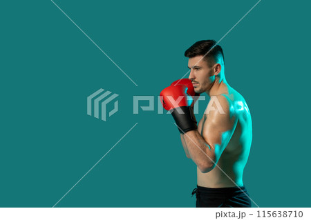 A man wearing boxing gloves strikes a dynamic pose on a vibrant green background. His stance exudes strength and determination as he showcases his boxing skills, copy space 115638710