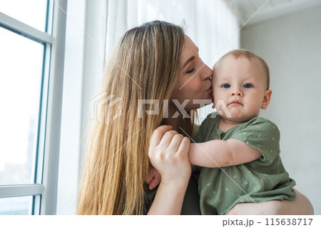 Happy family at home. Mother holding little toddler child daughter. Mom and baby girl relax playing having fun together at home. Mother hugging kissing baby with love care. Mom of breast feeding baby 115638717