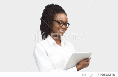 Smiling young African American businesswoman using a digital tablet, isolated on a white background. Business app concept Smiling young African American businesswoman using a digital tablet, isolated on a white background. Business app concept 115638810
