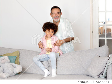 Grandpa And Grandson Bond. Happy Hispanic Grandfather Hugging And Cuddling With Grandchild Boy On Sofa At Home Interior, Smiling To Camera. Multigenerational Family Connection And Love 115638824