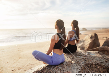Calm glad young caucasian women enjoy morning workout, breathing exercises, meditation, practice yoga in lotus position on sea beach. Sports outdoor, peace, lifestyle and body care Calm glad young caucasian women enjoy morning workout, breathing exercises, meditation, practice yoga in lotus position on sea beach. Sports outdoor, peace, lifestyle and body care 115639234