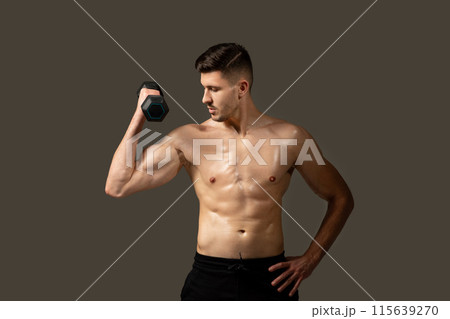 A shirtless man is seen holding a dumbbell in a gym setting. He appears focused and engaged in his workout routine, displaying strength and determination. A shirtless man is seen holding a dumbbell in a gym setting. He appears focused and engaged in his workout routine, displaying strength and determination. 115639270
