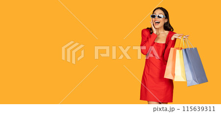 A woman dressed in a vibrant red dress stands holding multiple shopping bags in her hands, showcasing a successful shopping trip, looking at copy space 115639311