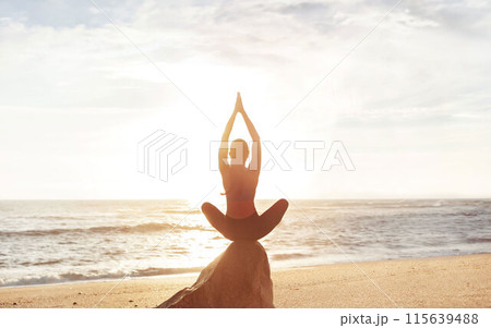 Calm young caucasian lady enjoy morning workout, breathing exercises, meditation, practicing yoga in lotus position on stone on sea beach. Lifestyle and body care, balance outdoor 115639488