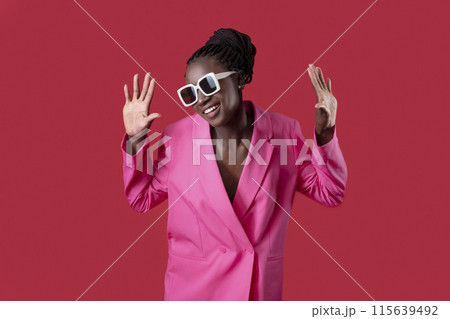 Portrait Of Young Black Female Fashion Model Wearing Pink Jacket And Stylish Sunglasses Posing Over Red Studio Background, Cheerful African American Woman Spreading Hands And Having Fun, Copy Space Portrait Of Young Black Female Fashion Model Wearing Pink Jacket And Stylish Sunglasses Posing Over Red Studio Background, Cheerful African American Woman Spreading Hands And Having Fun, Copy Space 115639492