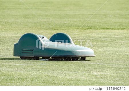 A battery-powered electric lawnmower drives across the field and cuts the grass. A battery-powered electric lawnmower drives across the field and cuts the grass. 115640242