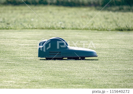 A battery-powered electric lawnmower drives across the field and cuts the grass. A battery-powered electric lawnmower drives across the field and cuts the grass. 115640272