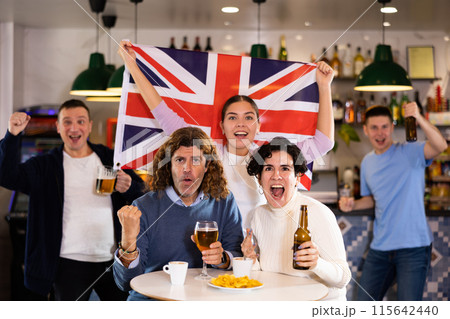 Company of joyful sports supporters waving flag of Great Britain and celebrating victory of favotite team in pub Company of joyful sports supporters waving flag of Great Britain and celebrating victory of favotite team in pub 115642440