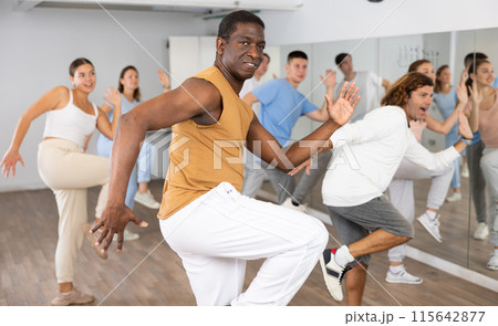 Excited multiethnic men and women exercising active moves with knee lifting in dance center indoors 115642877