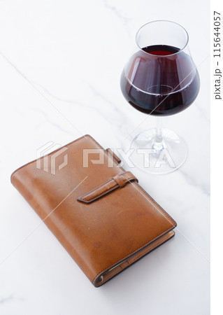 茶色の革のシステム手帳と赤ワインのグラス 115644057