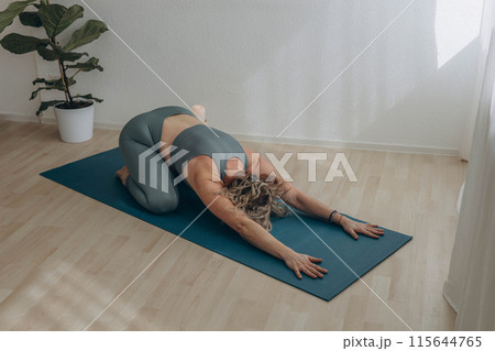 A 50-year-old woman does yoga at home 115644765