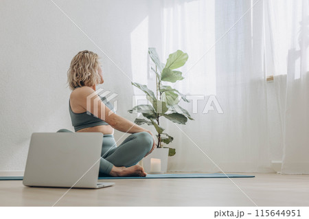 A 50-year-old woman does yoga at home 115644951