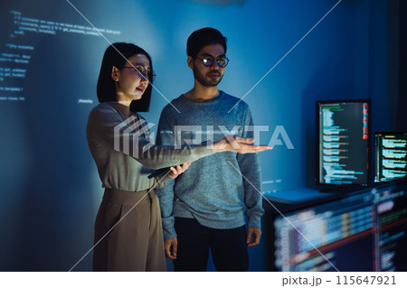 Asian Two software developers engaged in collaborative coding session, with code projected onto the wall and multiple computer screens displaying 115647921