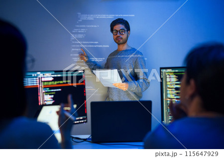 asian developer leads present code review session, pointing at code projected on the wall with colleagues  teamwork and knowledge sharing in software development. 115647929