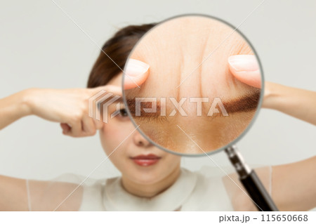 ルーペで女性の眉間のシワを拡大している. 115650668