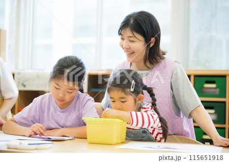 学童や放課後デイサービス等で絵を描く勉強をする先生と生徒　小学生複数と見守る先生 115651918