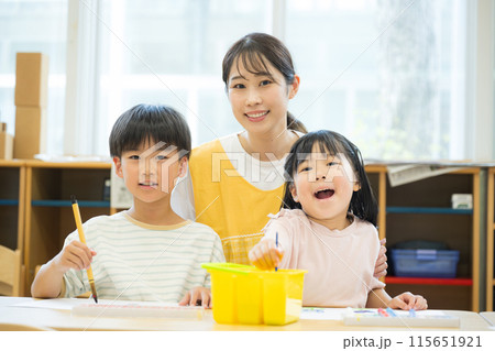 学童や放課後デイサービス等で勉強をする先生と生徒　小学生複数と先生のカメラ目線 115651921