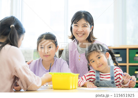 学童や放課後デイサービス等で勉強をする先生と生徒 小学生複数と先生のカメラ目線 学童や放課後デイサービス等で勉強をする先生と生徒 小学生複数と先生のカメラ目線 115651925