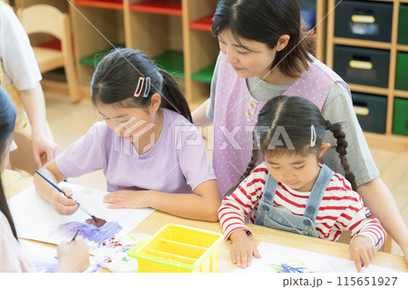 学童や放課後デイサービス等で勉強をする先生と生徒 小学生複数と見守る先生のクローズアップの俯瞰 学童や放課後デイサービス等で勉強をする先生と生徒 小学生複数と見守る先生のクローズアップの俯瞰 115651927