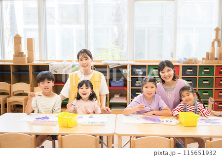 学童や放課後デイサービス等で勉強をする先生と生徒　小学生複数と先生のカメラ目線広角 115651932