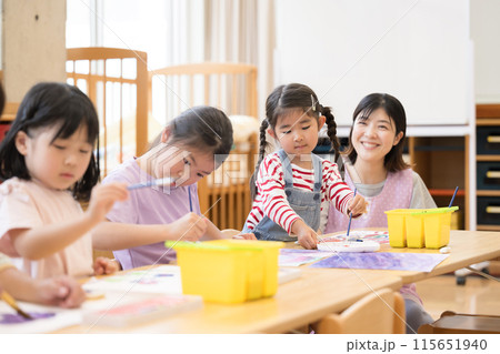 学童や放課後デイサービス等で勉強をする先生と生徒　小学生複数笑顔で見守る先生	 115651940