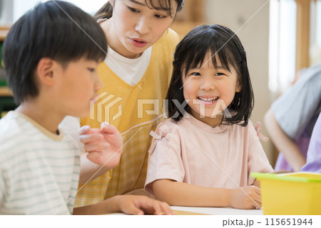 学童や放課後デイサービス等で勉強をする先生と生徒　小学生複数　カメラ目線の笑顔 115651944