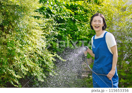 庭の緑に水やりをする笑顔のミドル女性 115653356