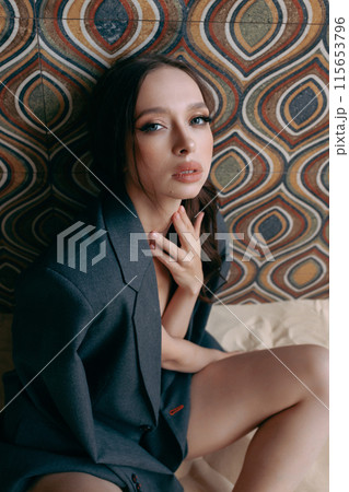 Woman in an unbuttoned jacket and jeans posing against a wall 115653796