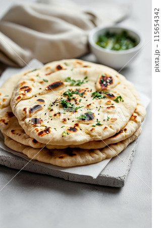 Delicious naan bread garnished with green herbs, served fresh and hot on a stone plate Delicious naan bread garnished with green herbs, served fresh and hot on a stone plate 115654342