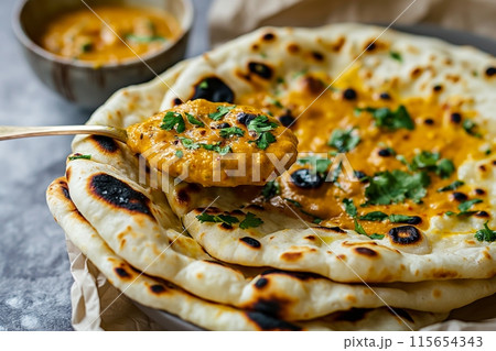 Hand scooping creamy curry with naan bread, highlighting traditional Indian flavors 115654343