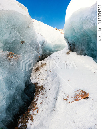 A stunning winter landscape on the way to Bogdanovich Glacier in Kazakhstan's Almaty Tian Shan Mountains. The path winds through a blue ice corridor adorned with mountain stones. 115654791