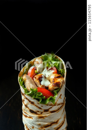 Succulent chicken and fresh vegetable wrap highlighted by a dark, elegant background Succulent chicken and fresh vegetable wrap highlighted by a dark, elegant background 115654795