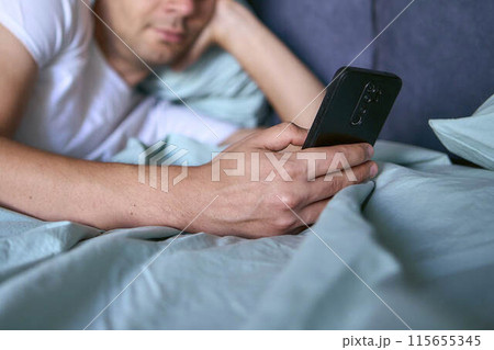 a young man scrolls in smartphone in the morning after waking up, morning routine 115655345